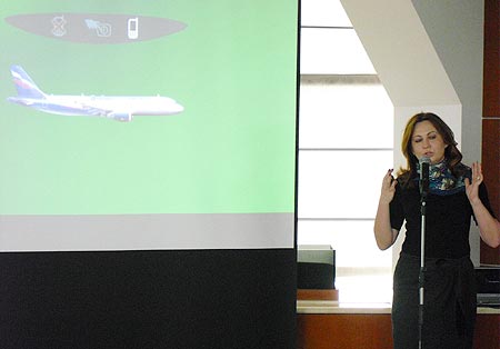 Коммерческий директор «Мегафона» Лариса Ткачук показывает салонное табло самолёта со значком «мобильная связь на борту включена»